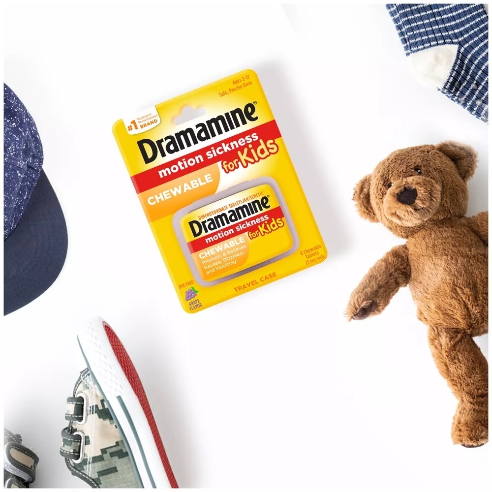Dramamine Kids packaging, surrounded by a child&#x27;s teddy bear, clothes, and sneaker