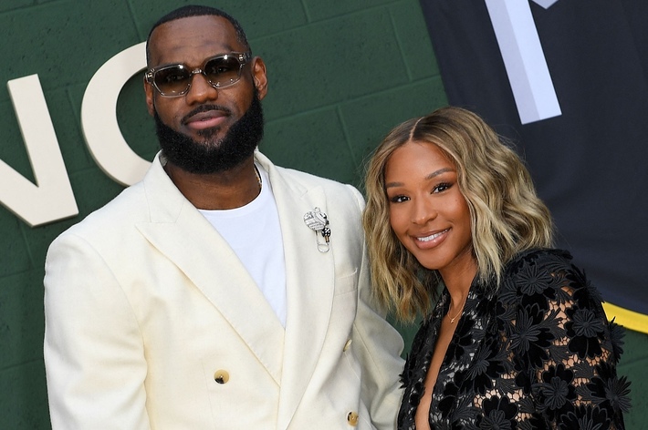 LeBron James in a white suit with a brooch next to a person in a black floral outfit