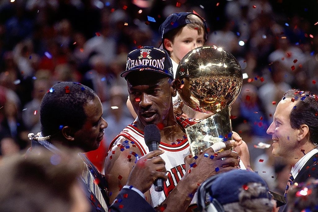 Michael Jordan celebrates with the NBA Championship trophy surrounded by teammates and confetti