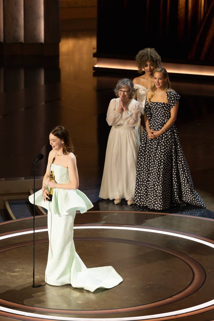 Emma Stone giving her acceptance speech as Sally Field and Jennifer Lawrence look on
