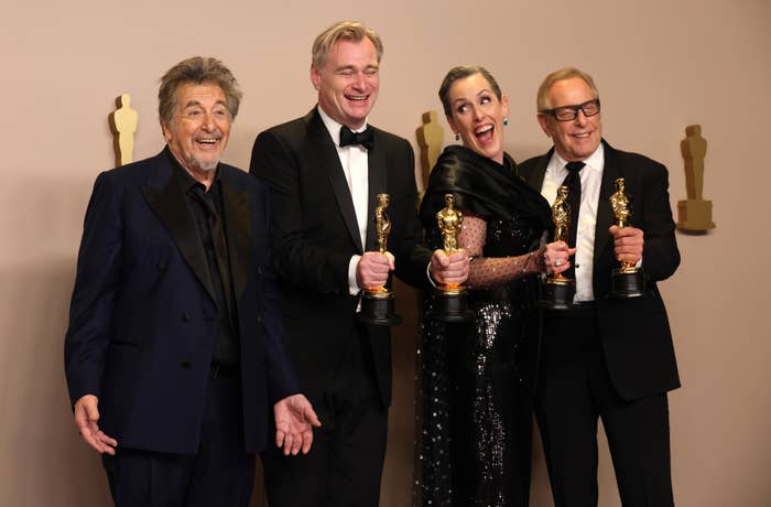 Christopher Nolan, Emma Thomas, and Charles Roven holding their Oscars while standing next to Al Pacino for photos