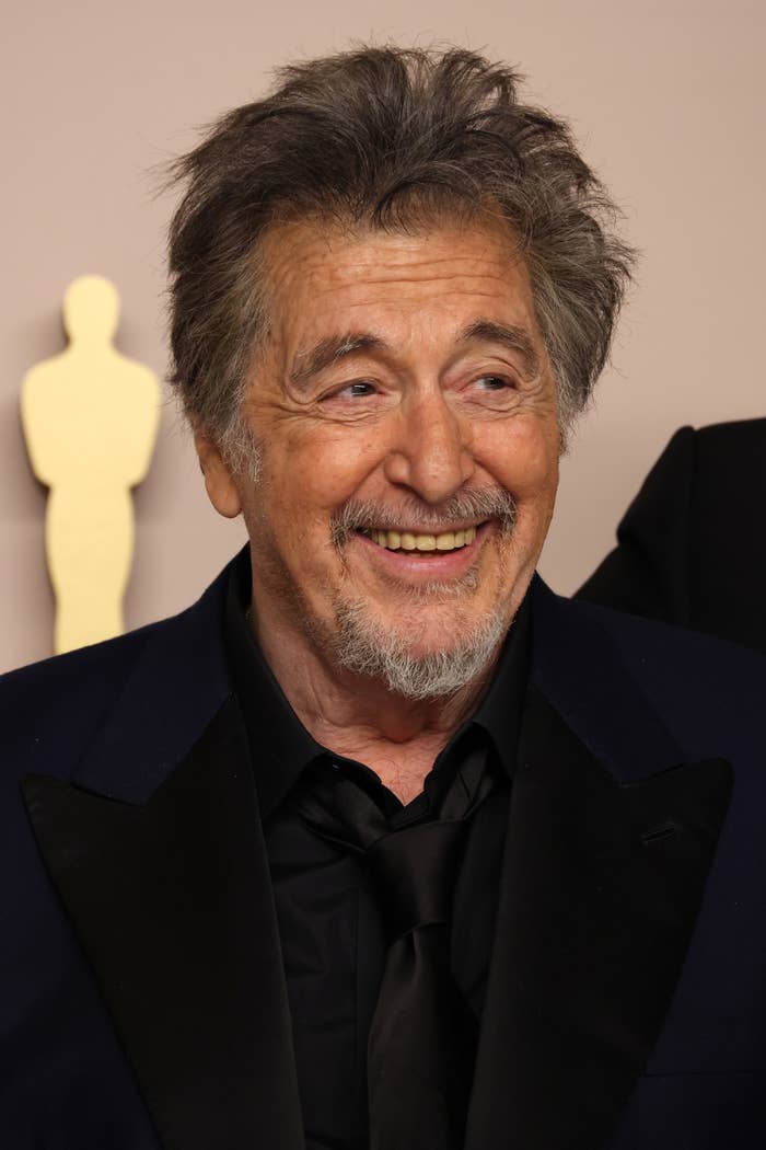 Al Pacino smiling in a tuxedo at a formal event with an award statue silhouette in the background