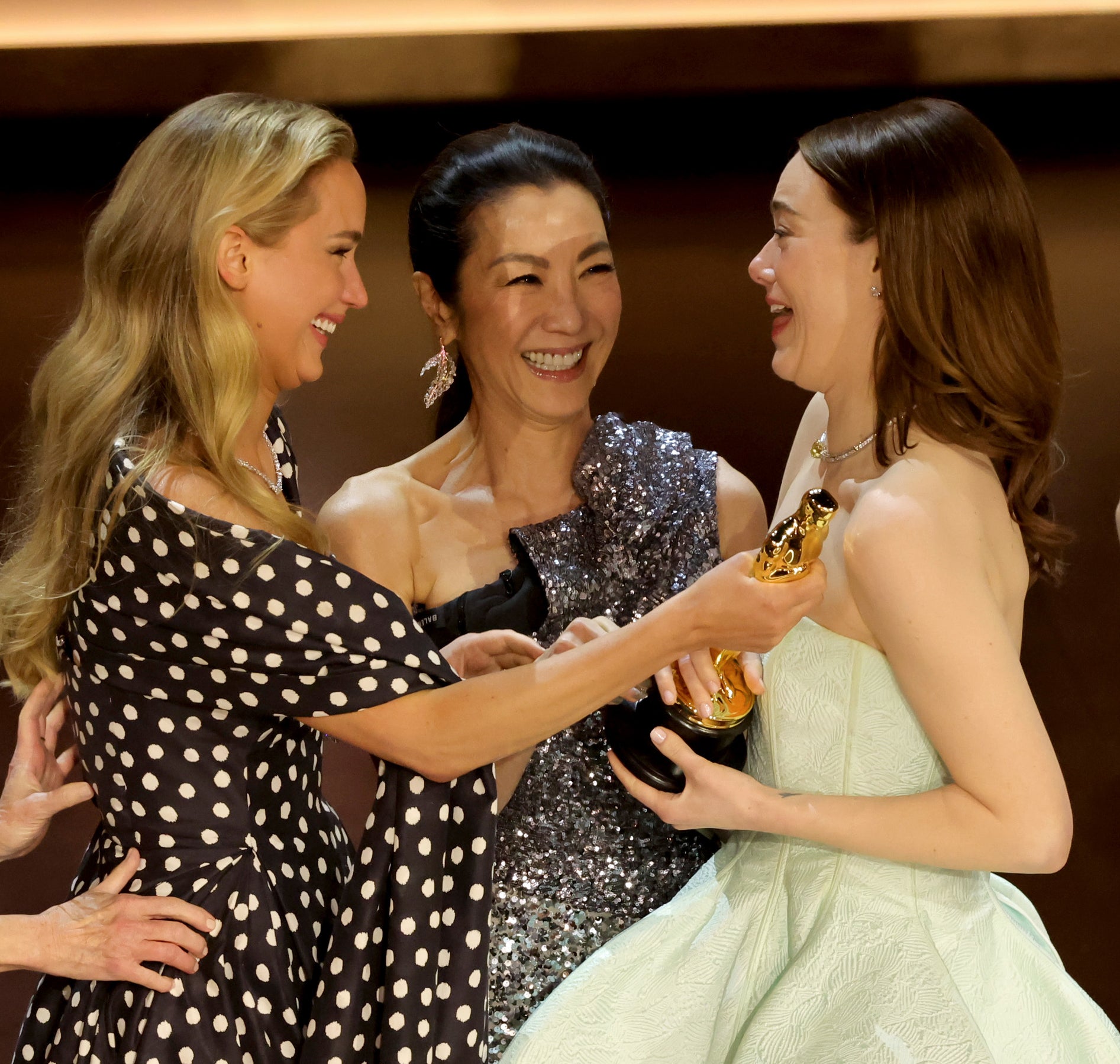 Jennifer Lawrence handing Emma Stone an Oscar while Michelle Yeoh looks on