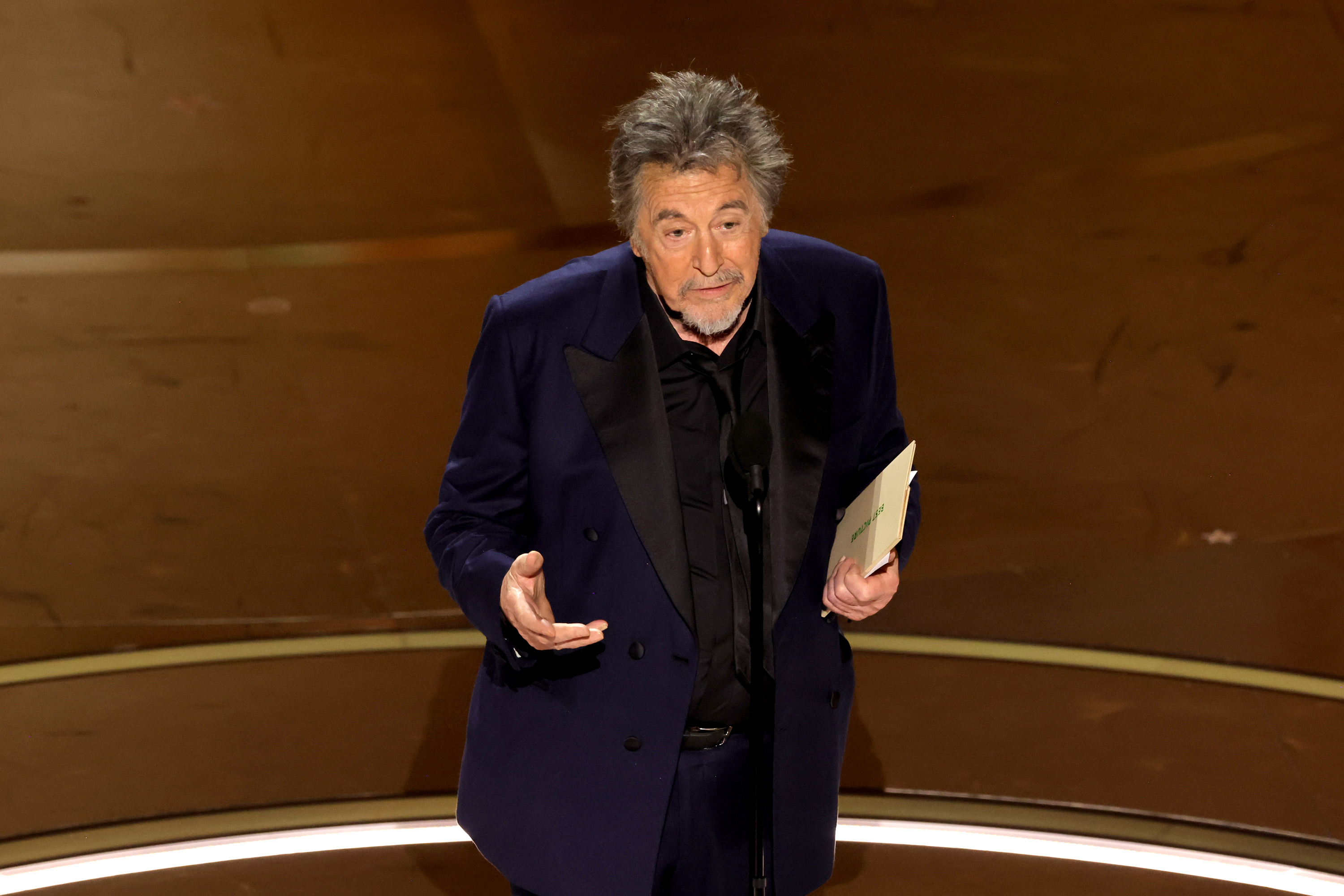Man in a dark suit presenting on stage at an awards ceremony