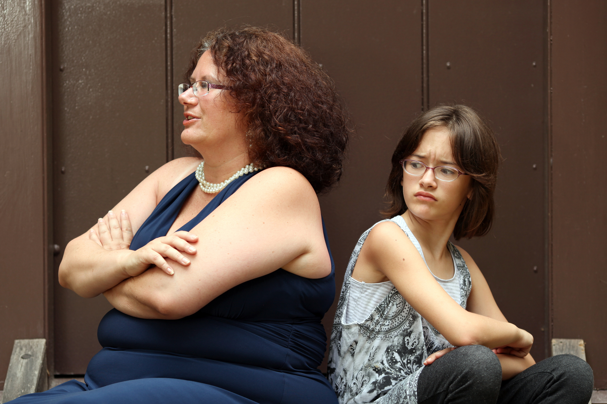 Woman and girl seated side by side, looking away with thoughtful expressions