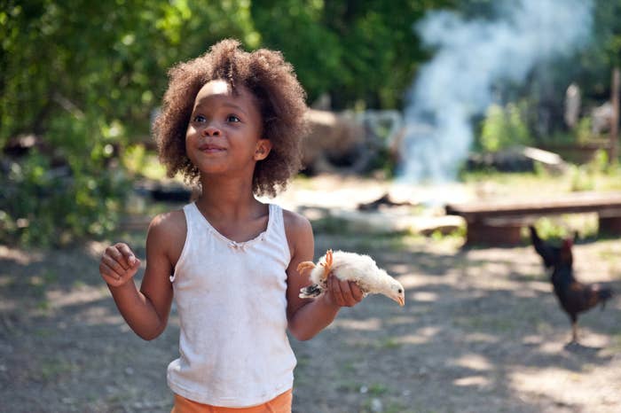 Hushpuppy smiling while standing outdoors and holding a small chicken