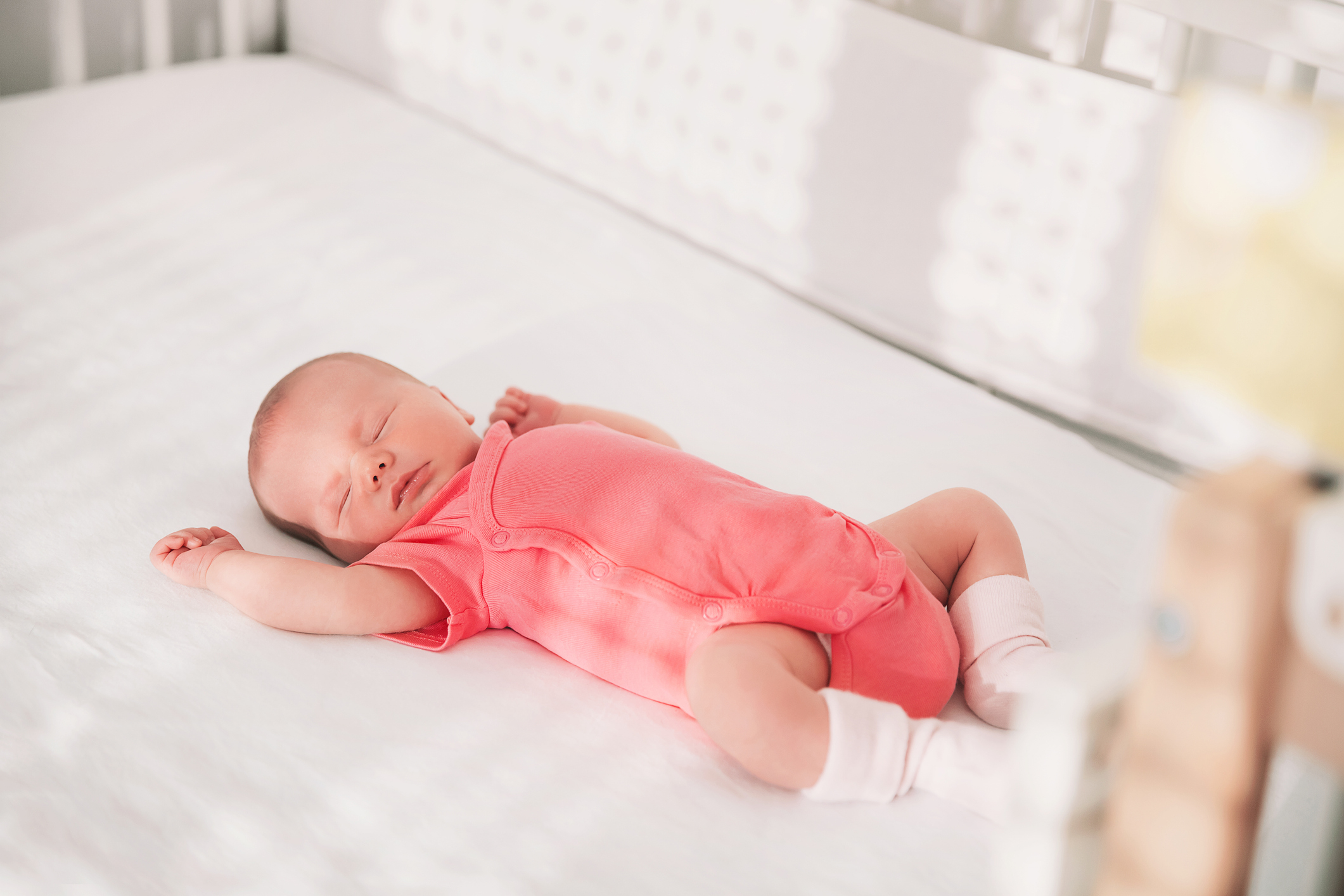 Infant sleeping peacefully on a crib mattress, dressed in a plain onesie