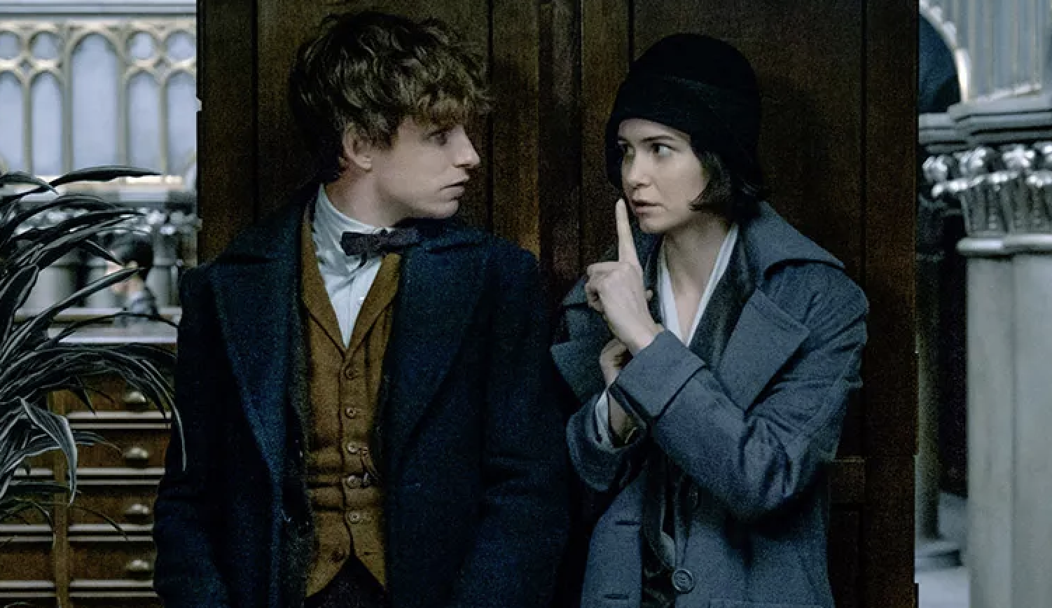 Two characters from &quot;Fantastic Beasts&quot; film series, Newt Scamander and Porpentina Goldstein, stand close in period attire, appearing in a discussion