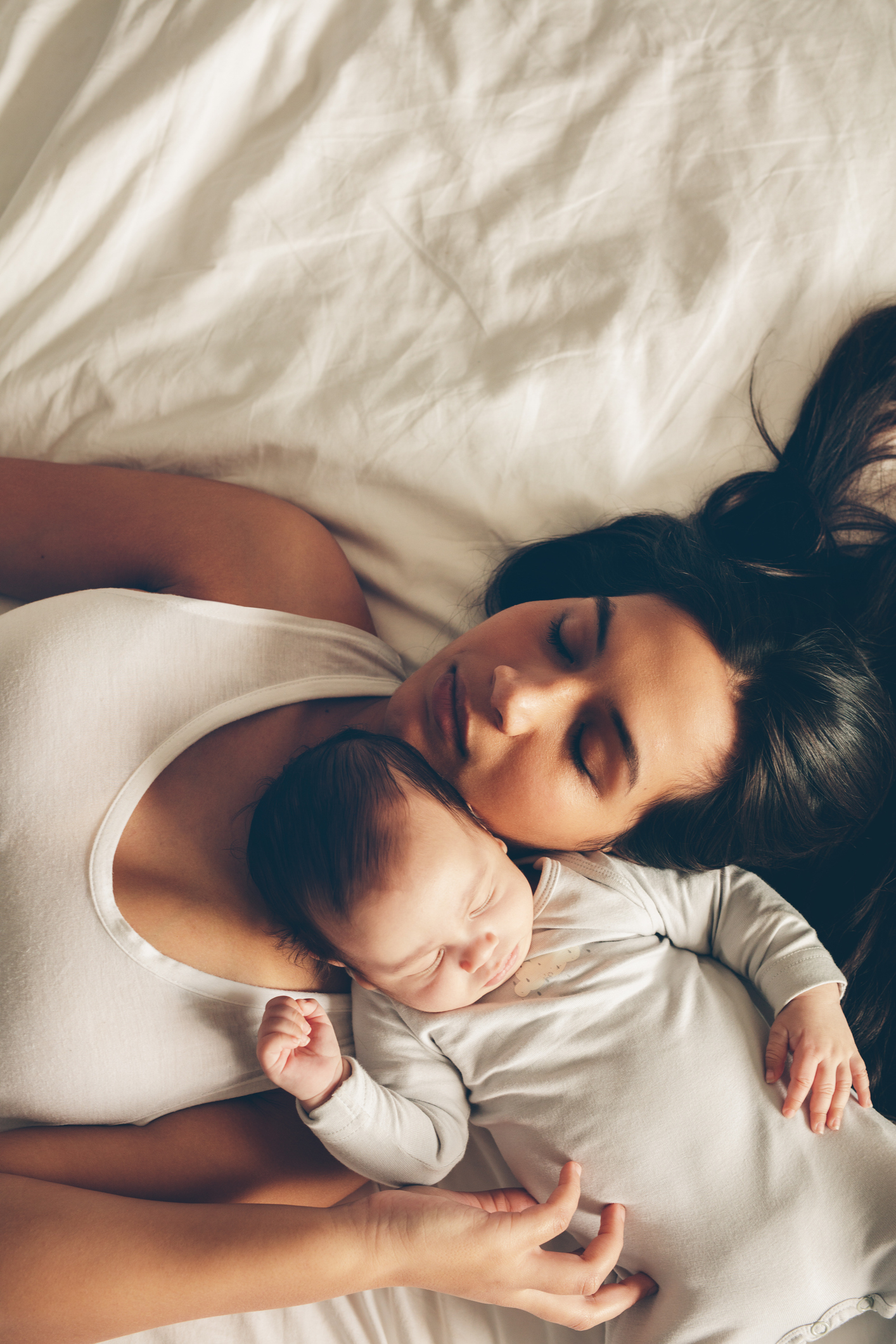 Woman lying down holding a sleeping baby. Both are relaxed and appear to be napping