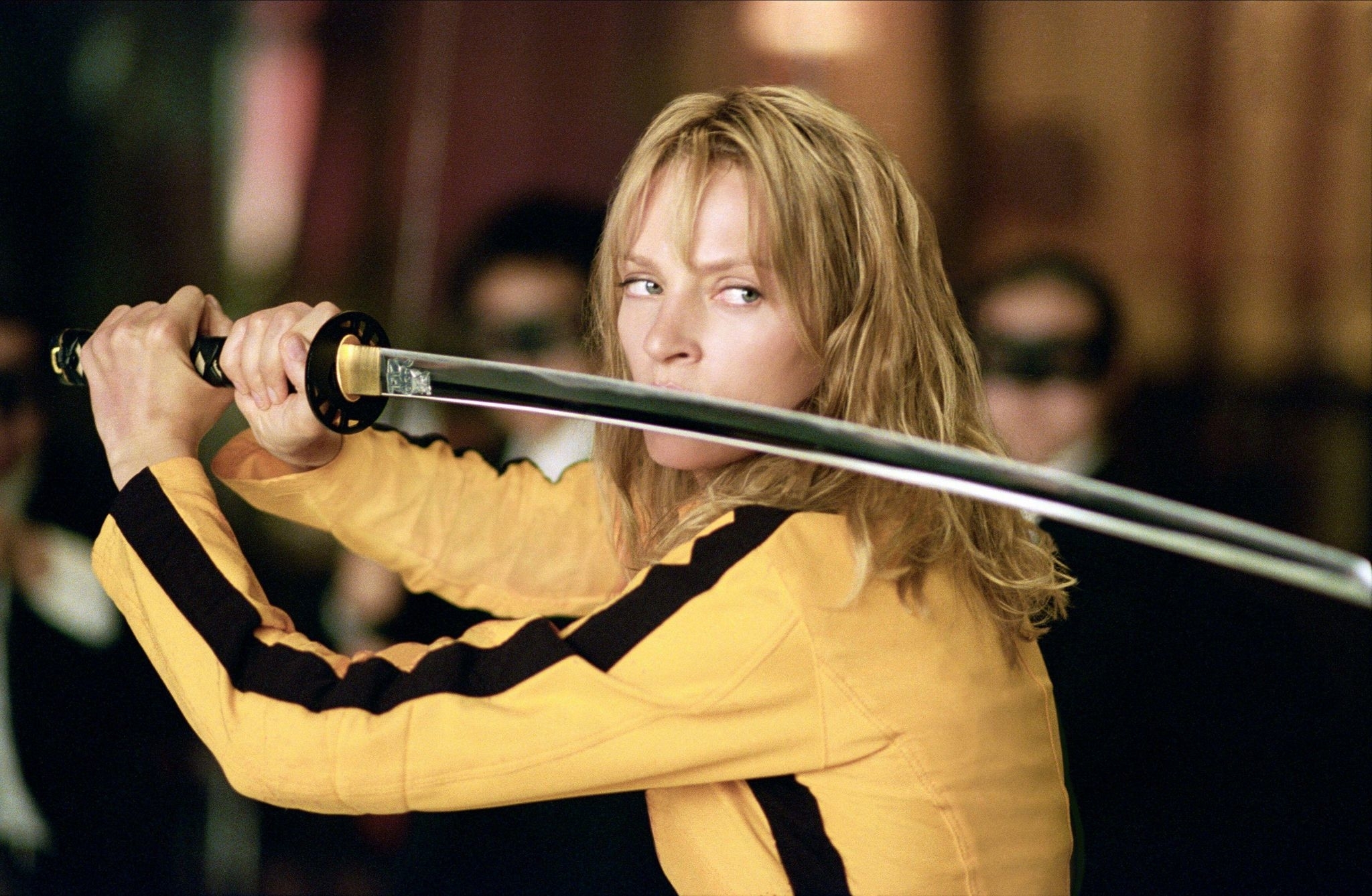 Uma Thurman in a yellow tracksuit wields a katana in a fighting stance from the film &#x27;Kill Bill.&#x27;
