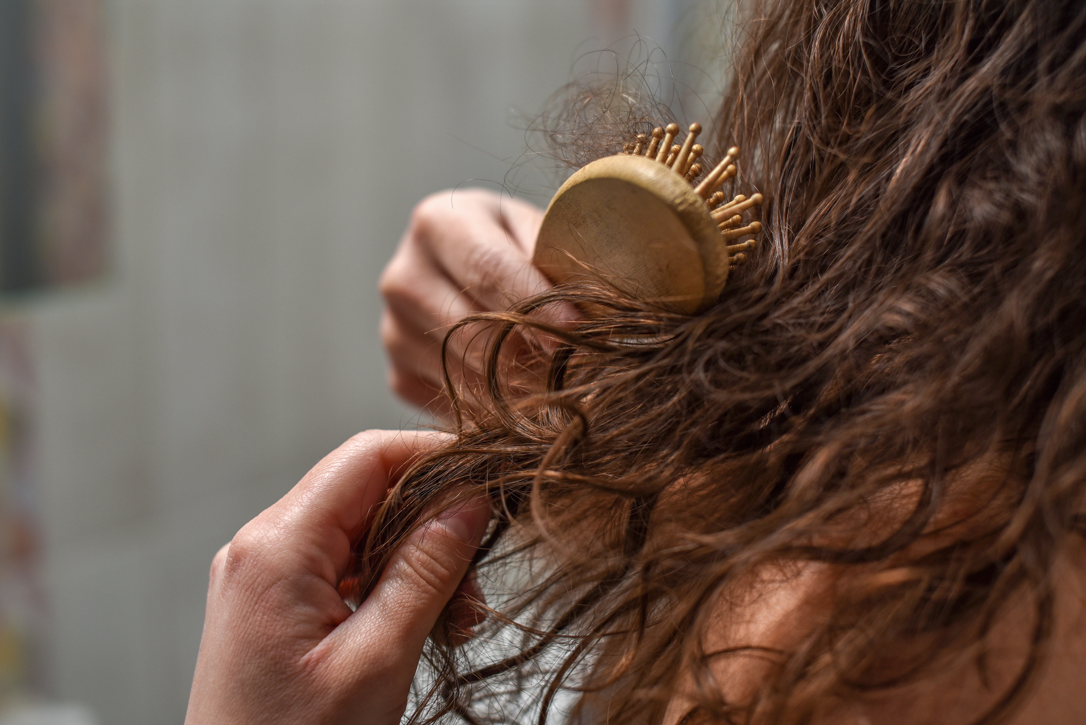 Person combing through curly hair with a round brush