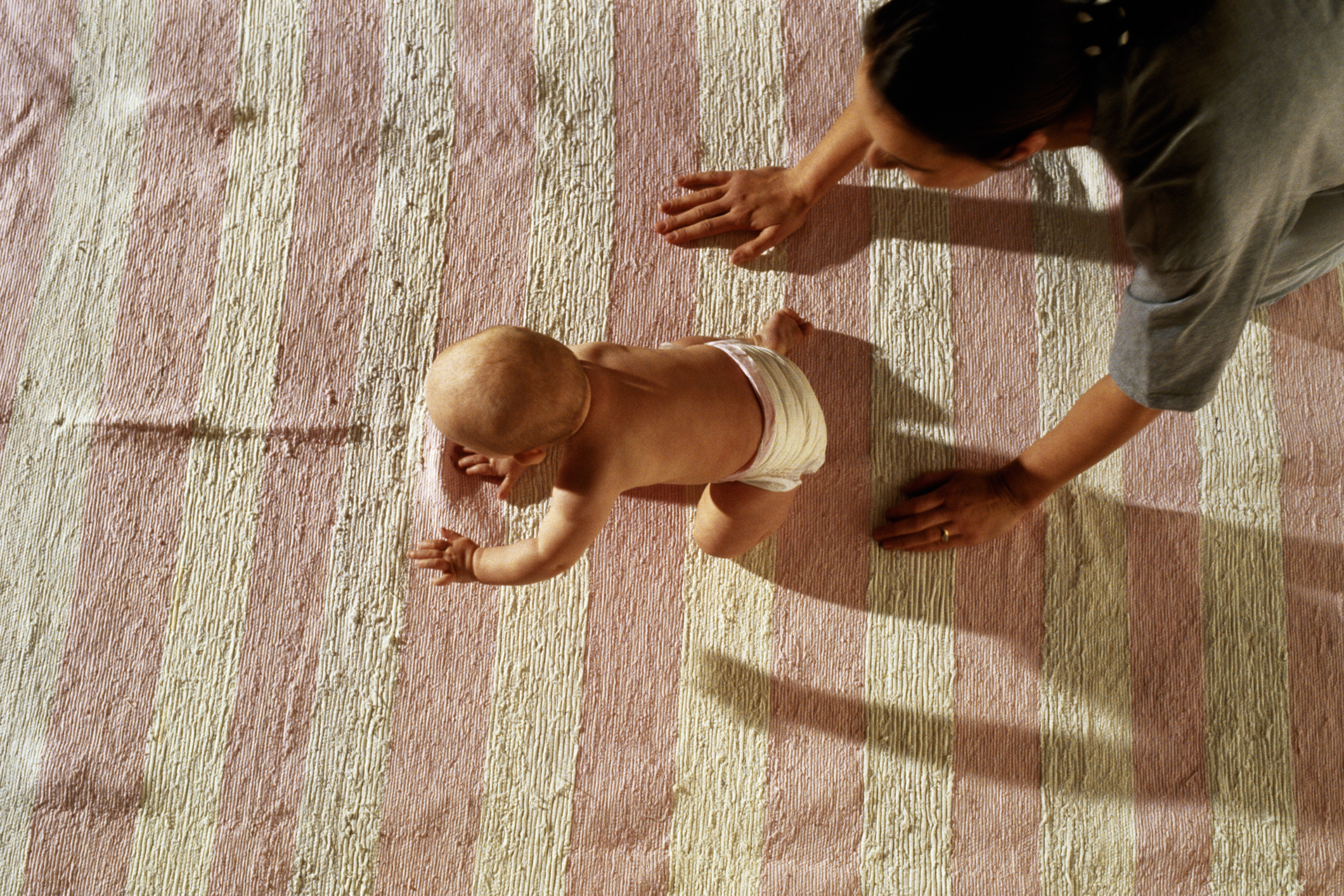 Adult supervising a baby crawling on a carpeted floor