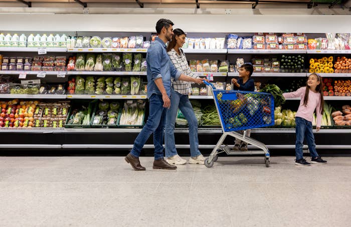 Family with a shopping cart picking out vegetables in a grocery store aisle