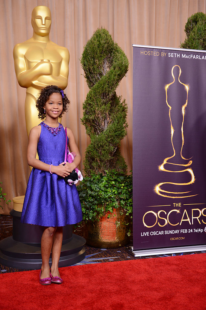 Quvenzhané Wallis in a purple dress holding a plush dog at the Oscars luncheon