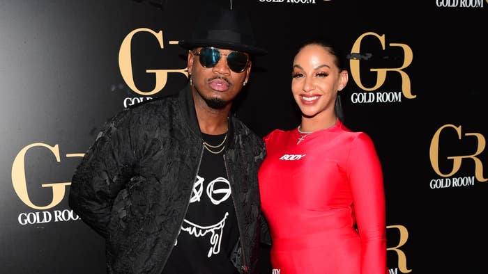 Ne-Yo and Crystal Renay standing together at an event. Ne-Yo is wearing a black textured outfit and a hat, and Crystal Renay in a sleek red dress