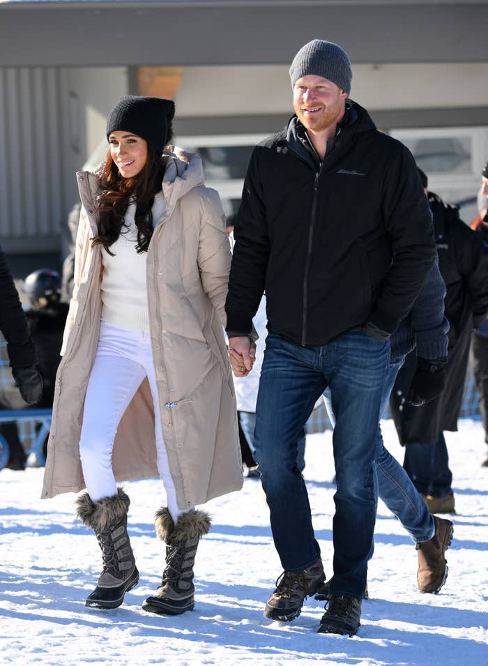 Meghan and Harry walk hand in hand in snow, wearing winter attire with hats and boots