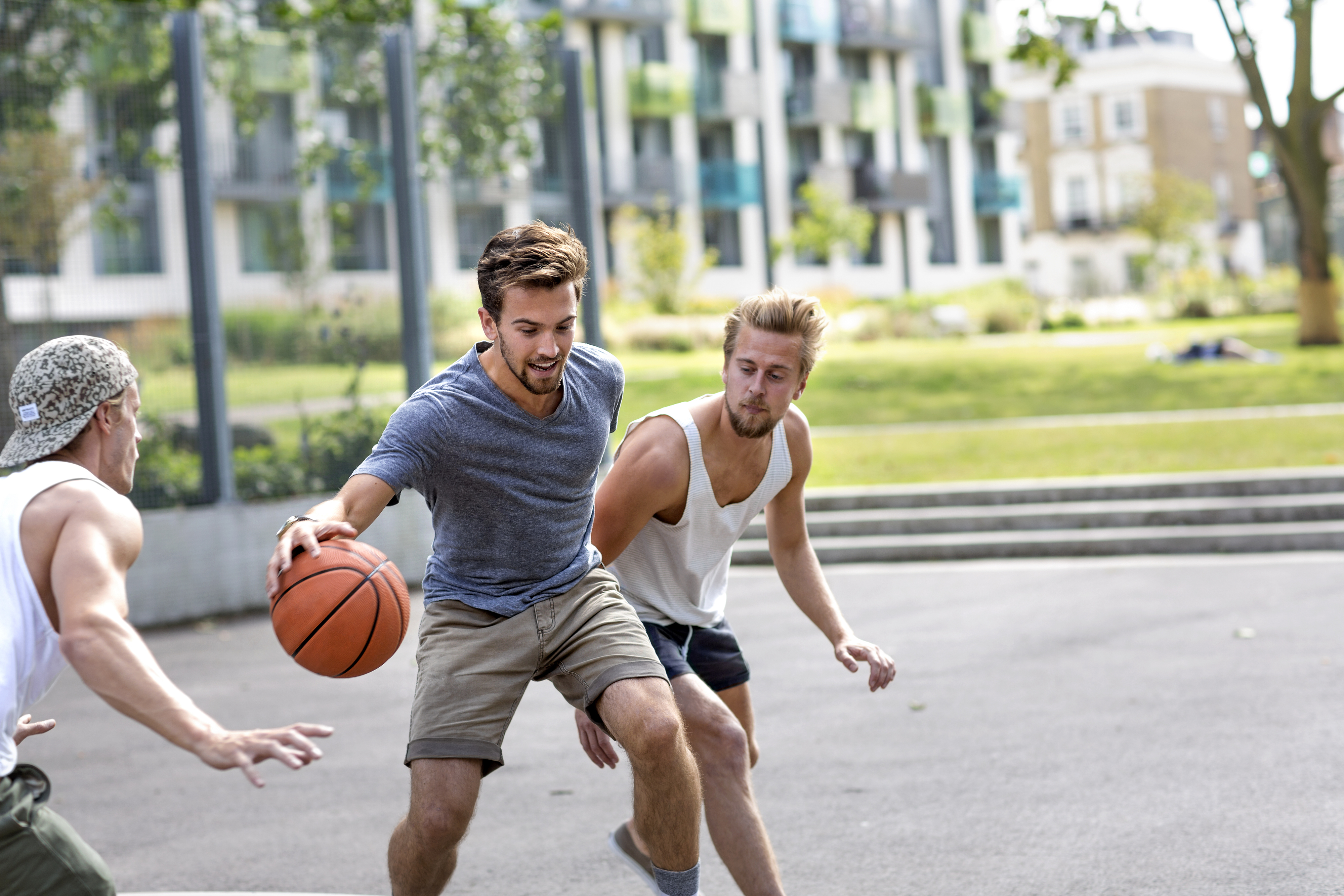Three individuals play basketball outdoors