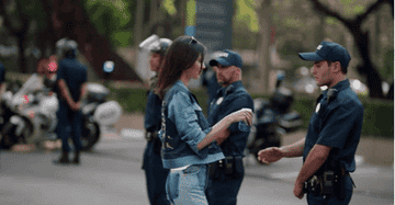 GIF of Kendall handing a cop a can, surrounded by individuals in police uniforms near motorcycles