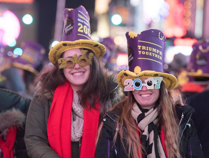 Two individuals wearing 2017 New Year&#x27;s Eve glasses and festive hats, smiling at a crowded event