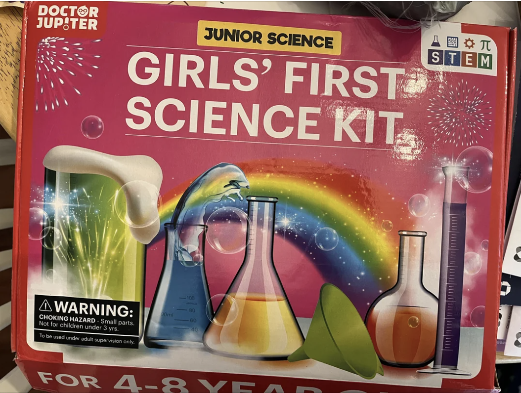 &quot;Science kit packaging titled &#x27;GIRLS&#x27; FIRST SCIENCE KIT&#x27; with illustrations of lab equipment and a rainbow.&quot;
