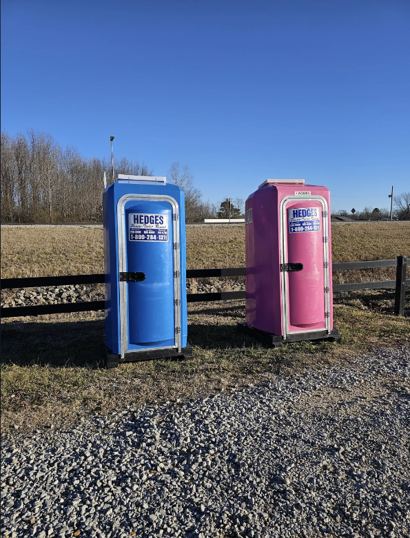 Two portable restrooms from Hedges, one blue and one pink, side by side in an open field