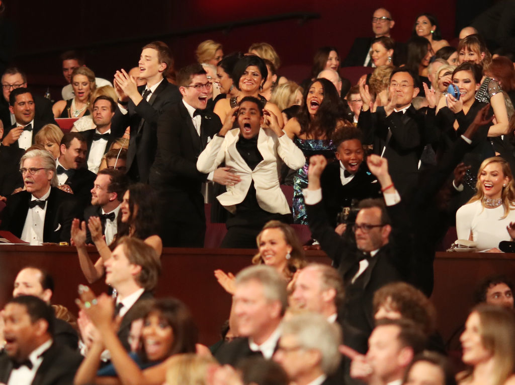 Audience members in formal attire applauding enthusiastically at an event