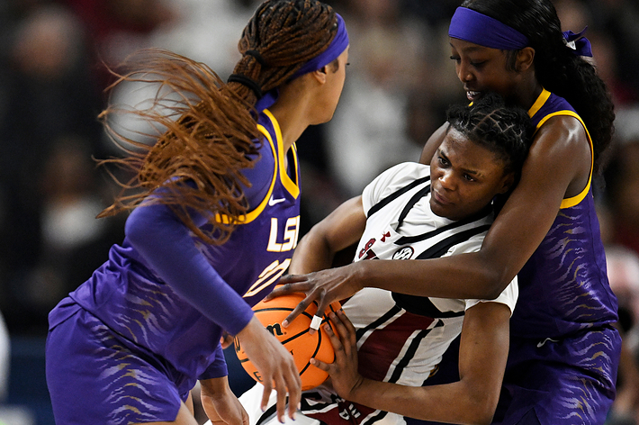 Three basketball players in action, one defending the ball against two opponents