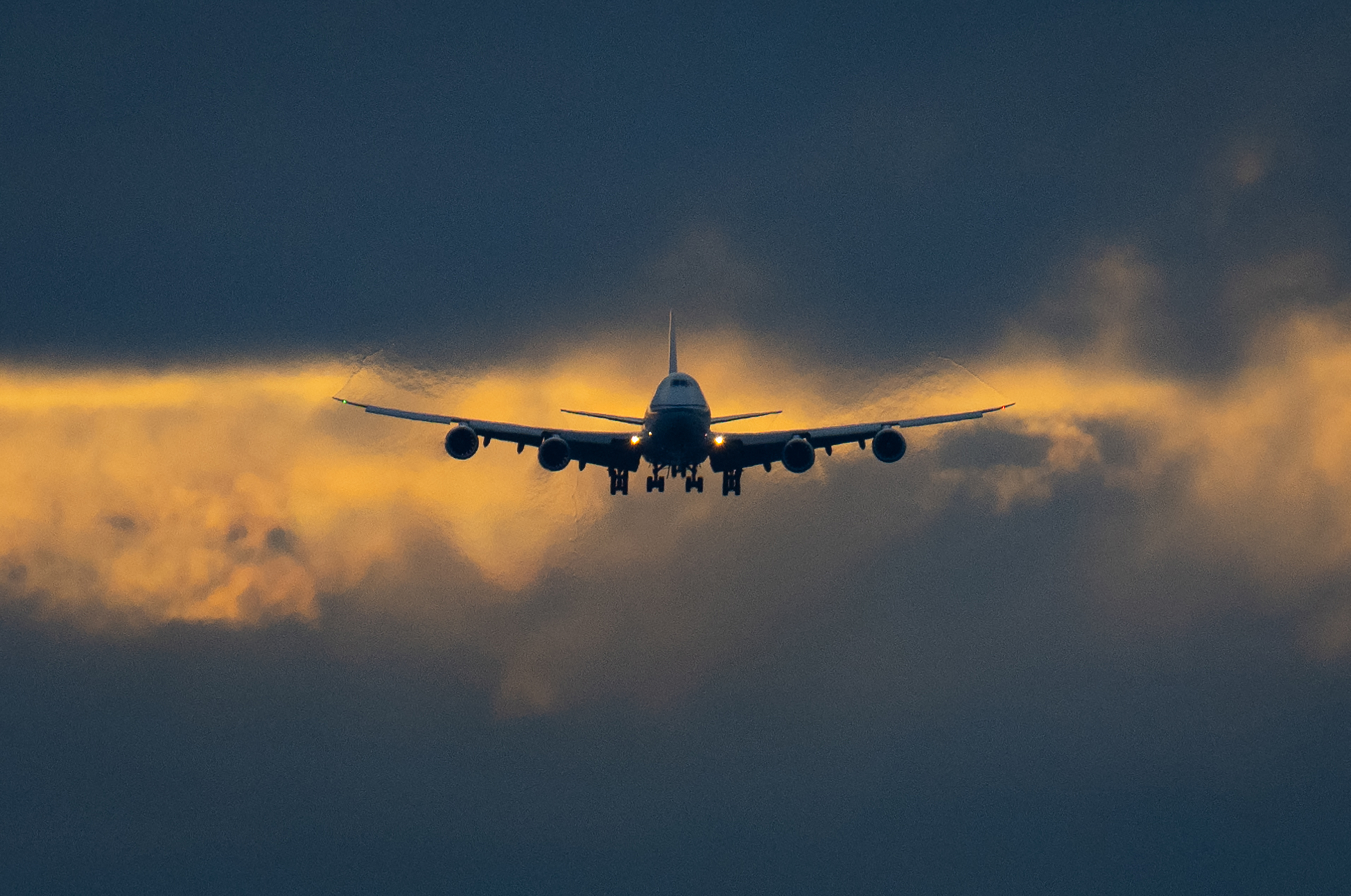 Airplane silhouetted against cloudy sky, with light from sunset visible in the background