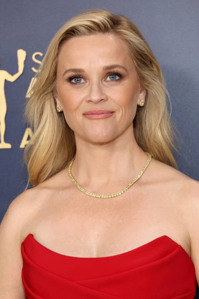 Reese Witherspoon smiling in an elegant off-shoulder dress at an event