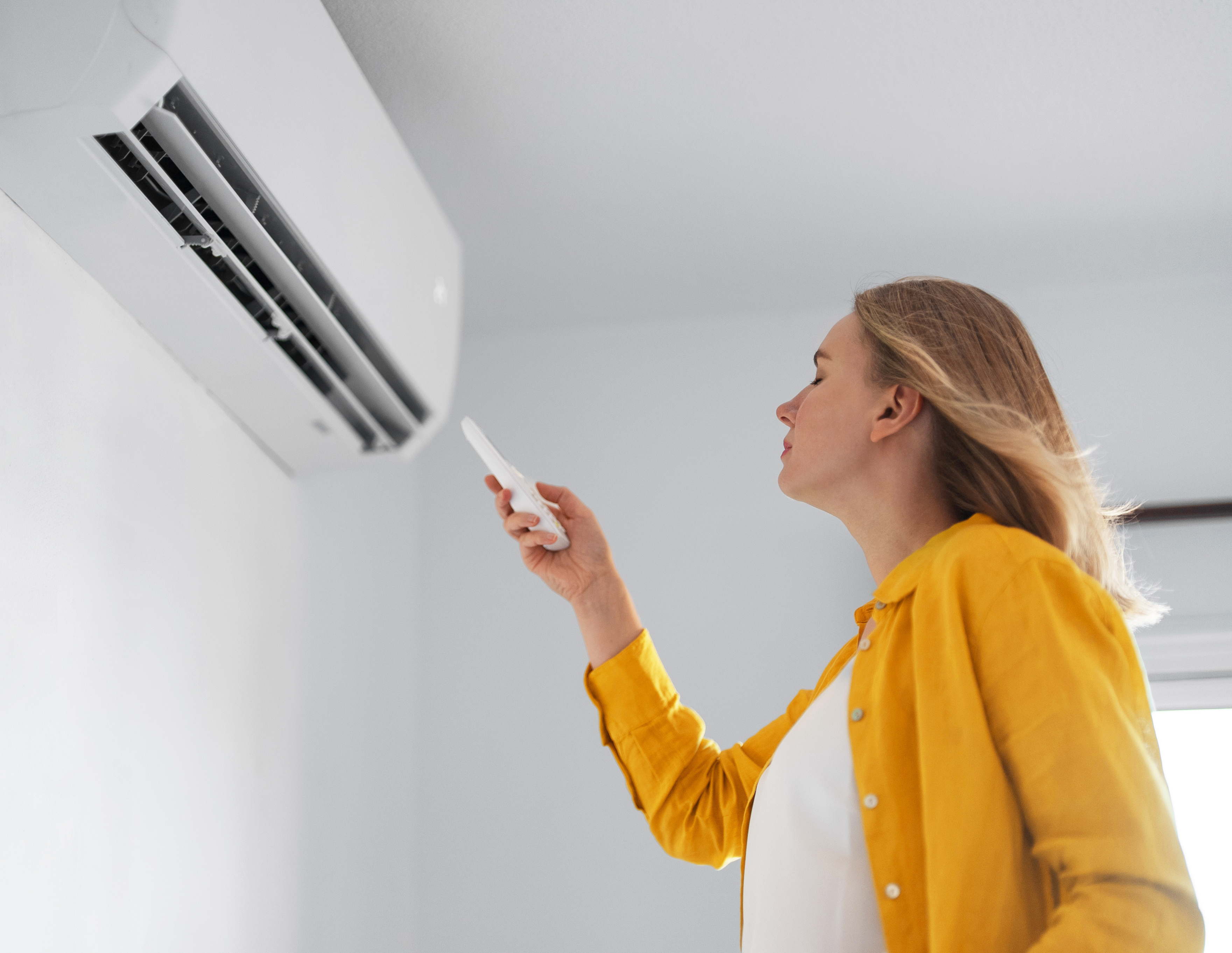 Woman using a remote to operate an air conditioning unit indoors