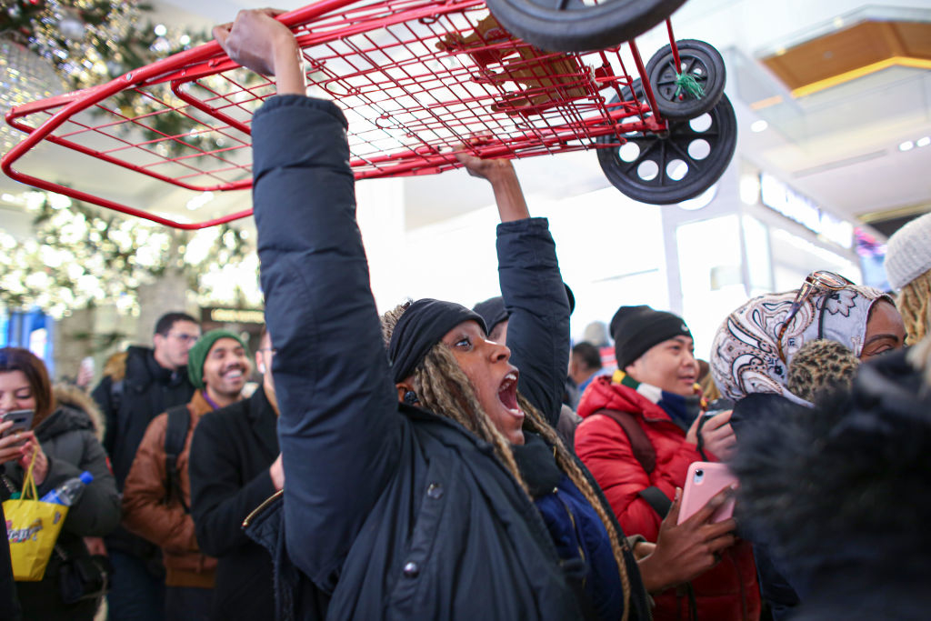 A person excitedly holds up a shopping cart above the crowd during a public event