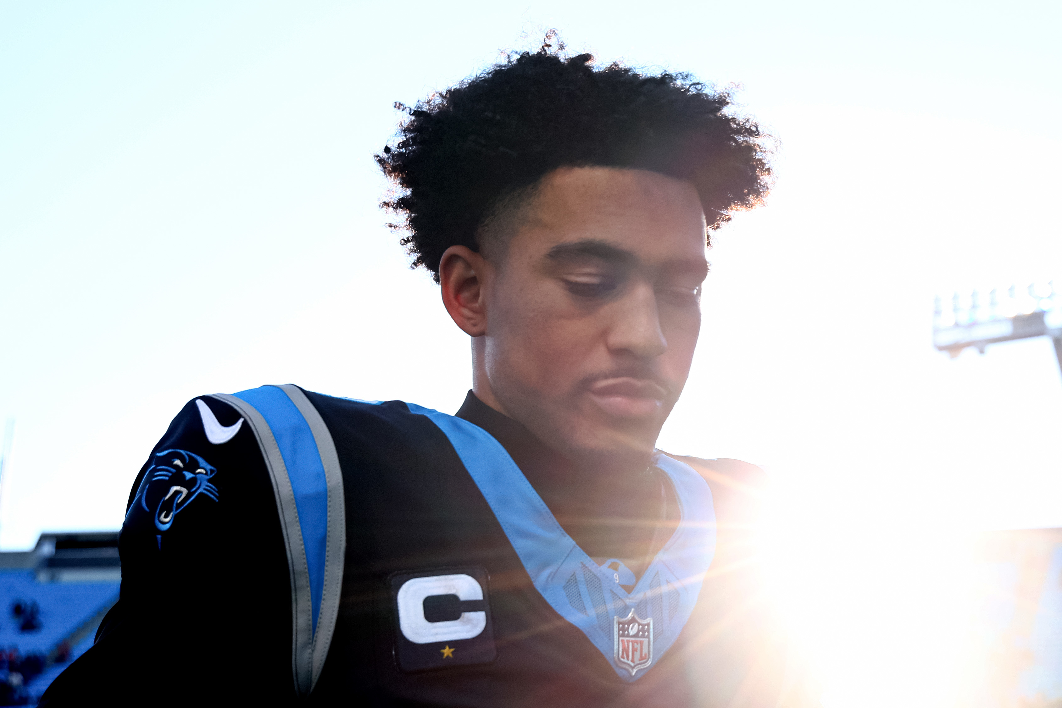 Football player in a jersey with a captain&#x27;s patch, standing in sunlight, introspective expression