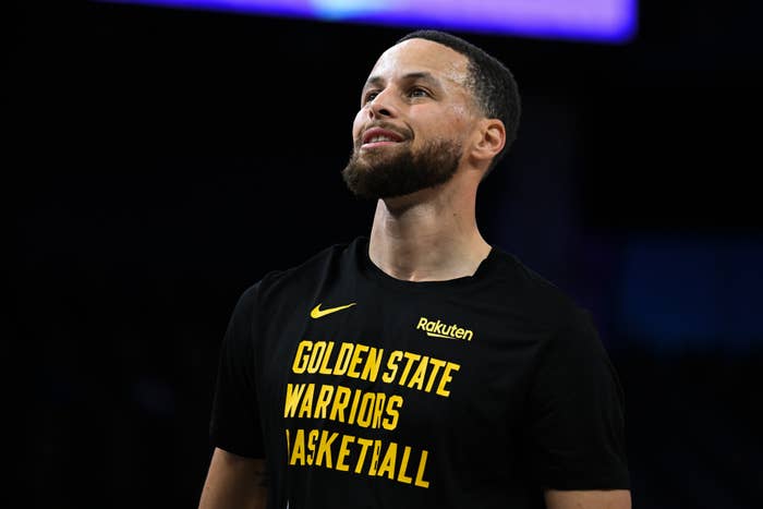 Stephen Curry in a Golden State Warriors shirt looks up with a confident smile