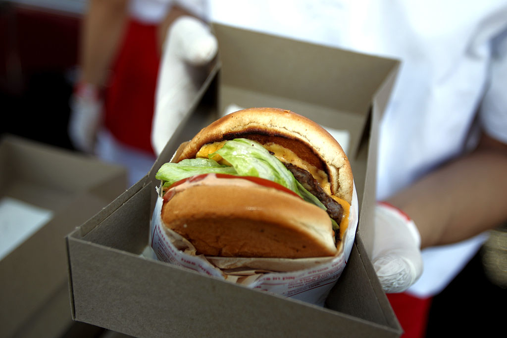Person holding a boxed burger with lettuce and tomato visible
