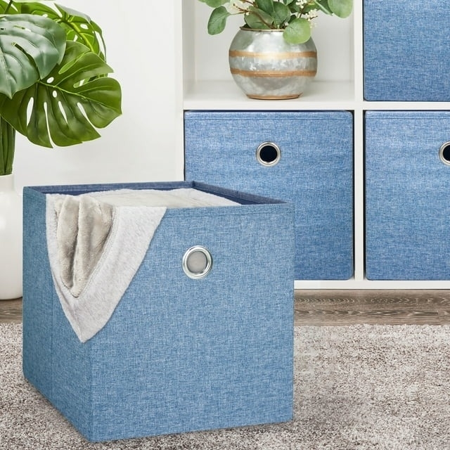 Foldable storage cube with metal ring handle and a blanket peeking out