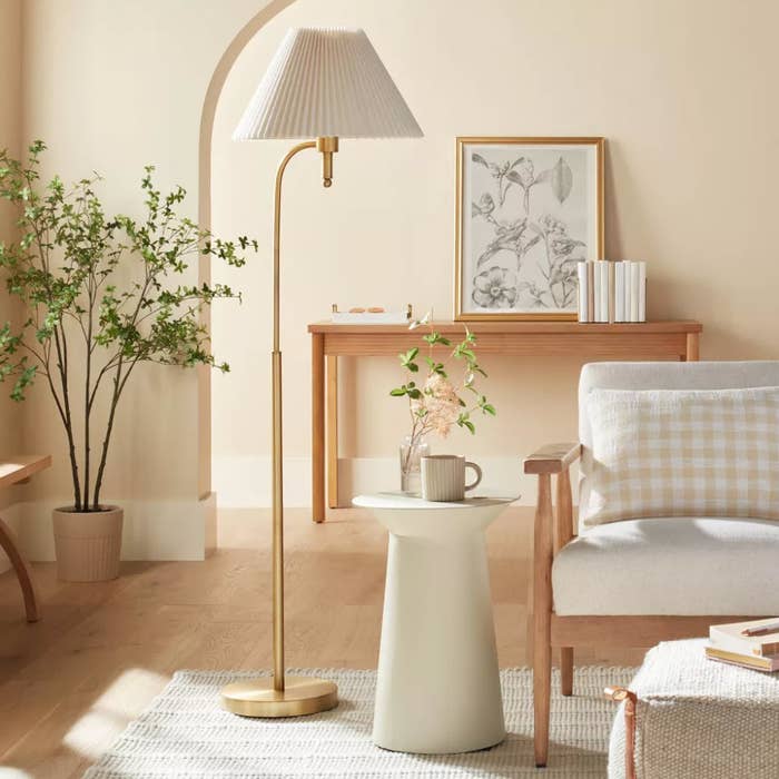 A minimalist living room with a floor lamp, artwork, plants, and a chair next to a small table