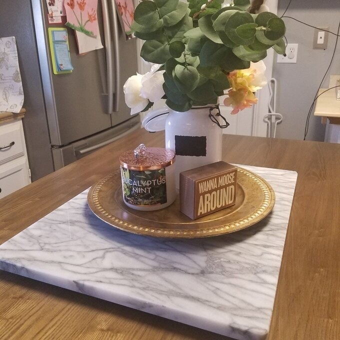 Scented candles on a marble tray on a wooden table with a vase of flowers, promoting a cozy home atmosphere
