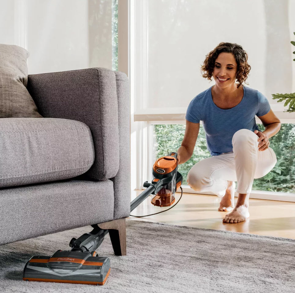 Woman using a cordless vacuum cleaner under a sofa in a living room