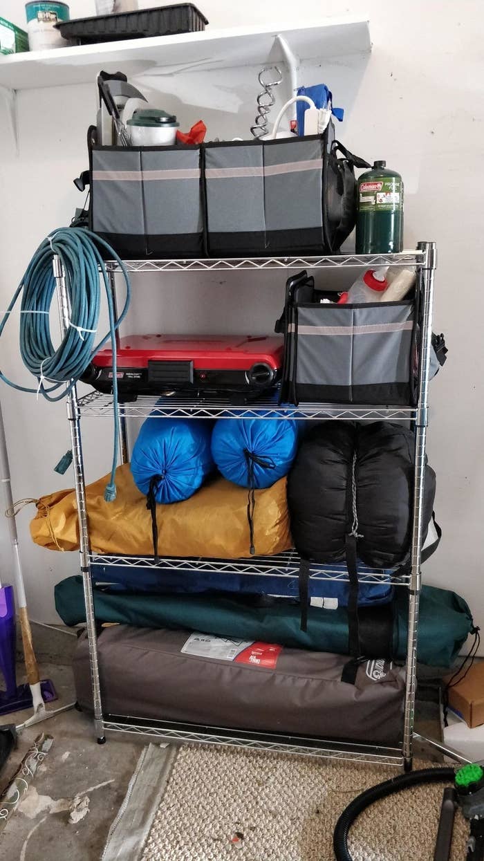 Metal storage shelf in a garage with various items, including bins, a hose, and camping gear
