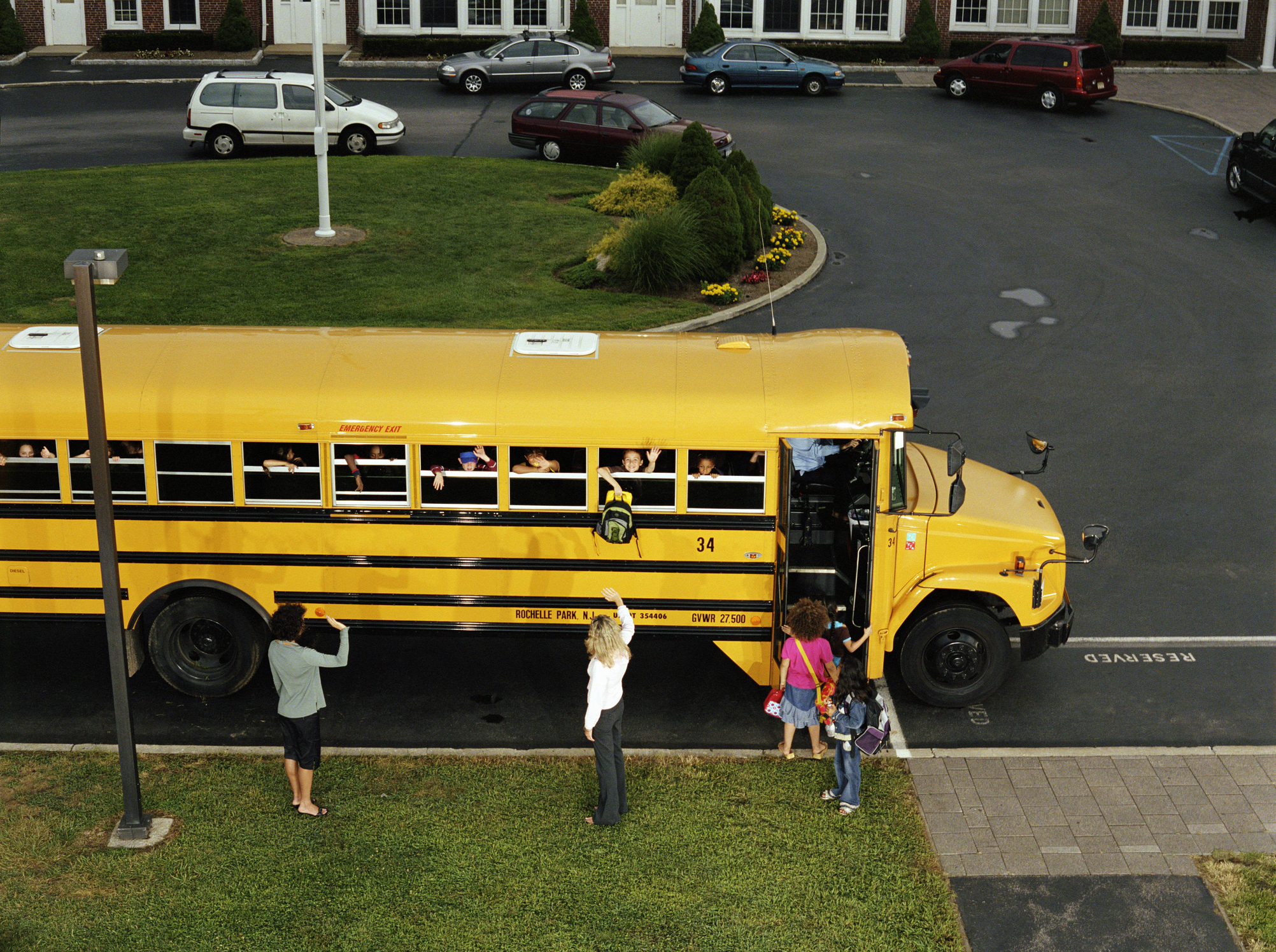 Schoolchildren waving from bus windows while adults greet them from the sidewalk