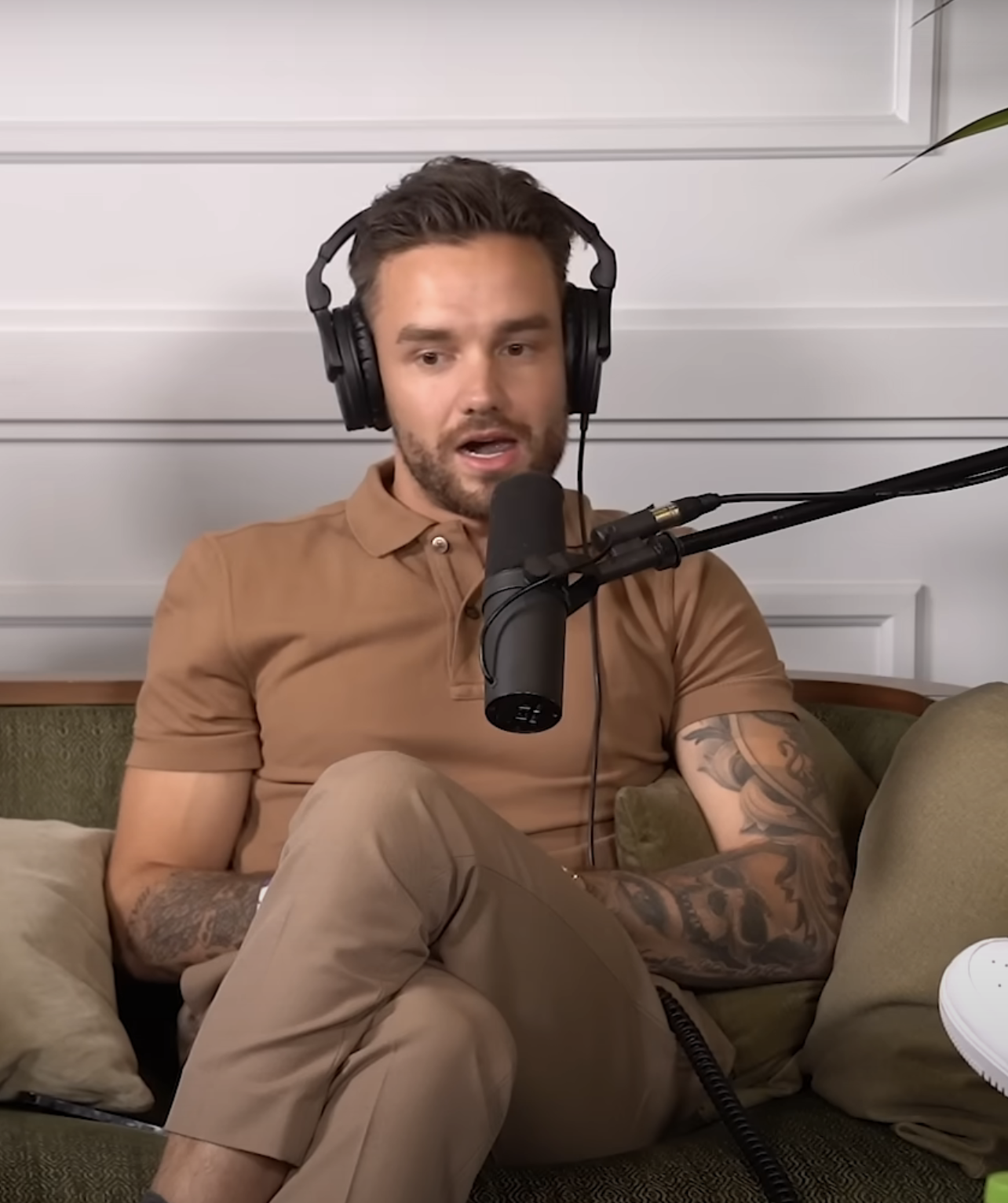Liam Payne wearing a polo shirt, seated with microphone and headphones, recording a podcast