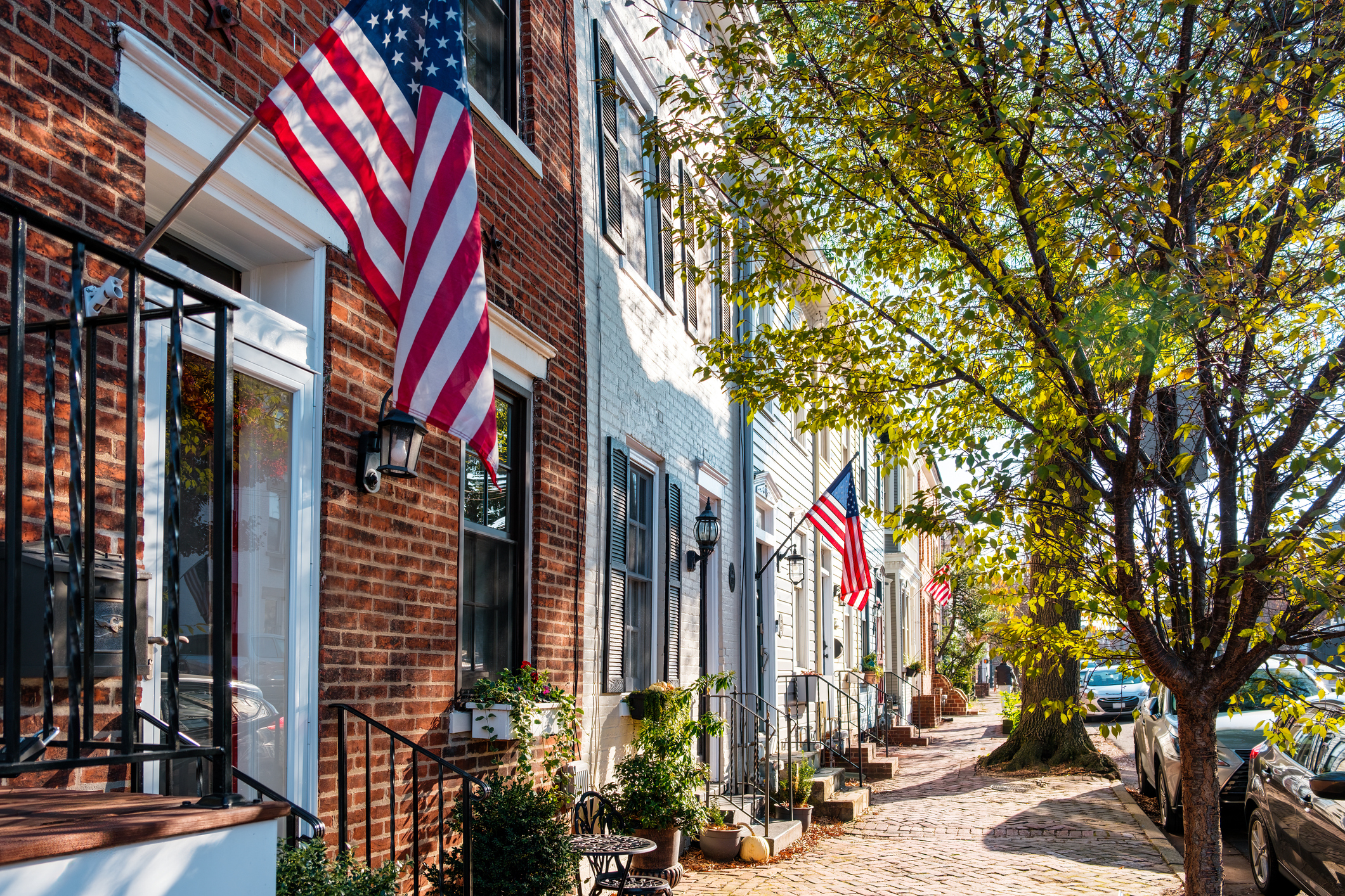 Quaint street with tree-lined sidewalk and brick townhouses displaying American flags