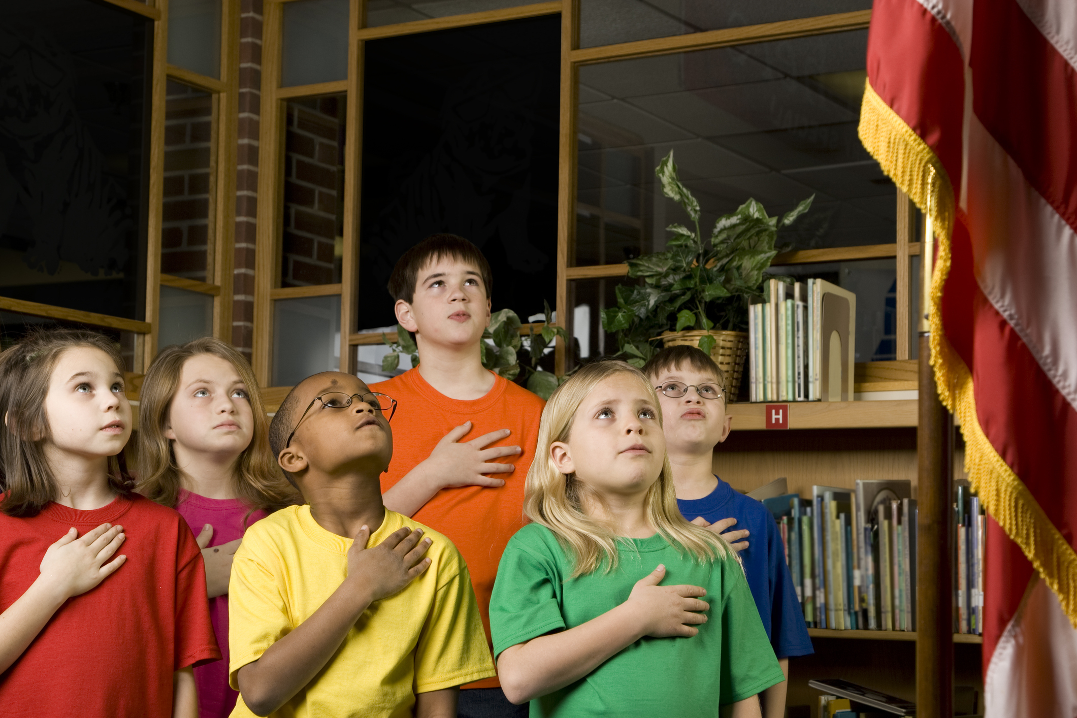 Group of children standing with hands over hearts looking upward in a library setting