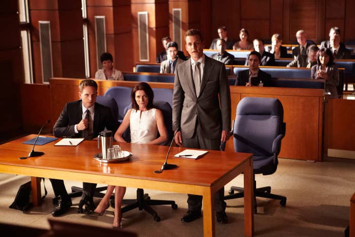Actors in a courtroom scene, standing and seated, portraying lawyers and a client in a TV drama