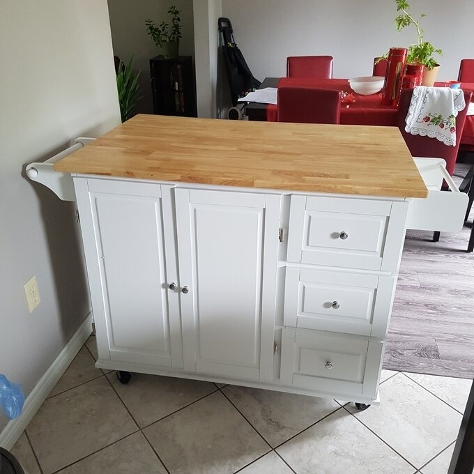 Portable kitchen island with wooden top, cabinet doors, and drawers in a home interior. Perfect for extra storage and meal prep space