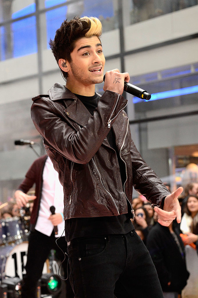 Zayn with microphone performing live, wearing leather jacket, fans in background