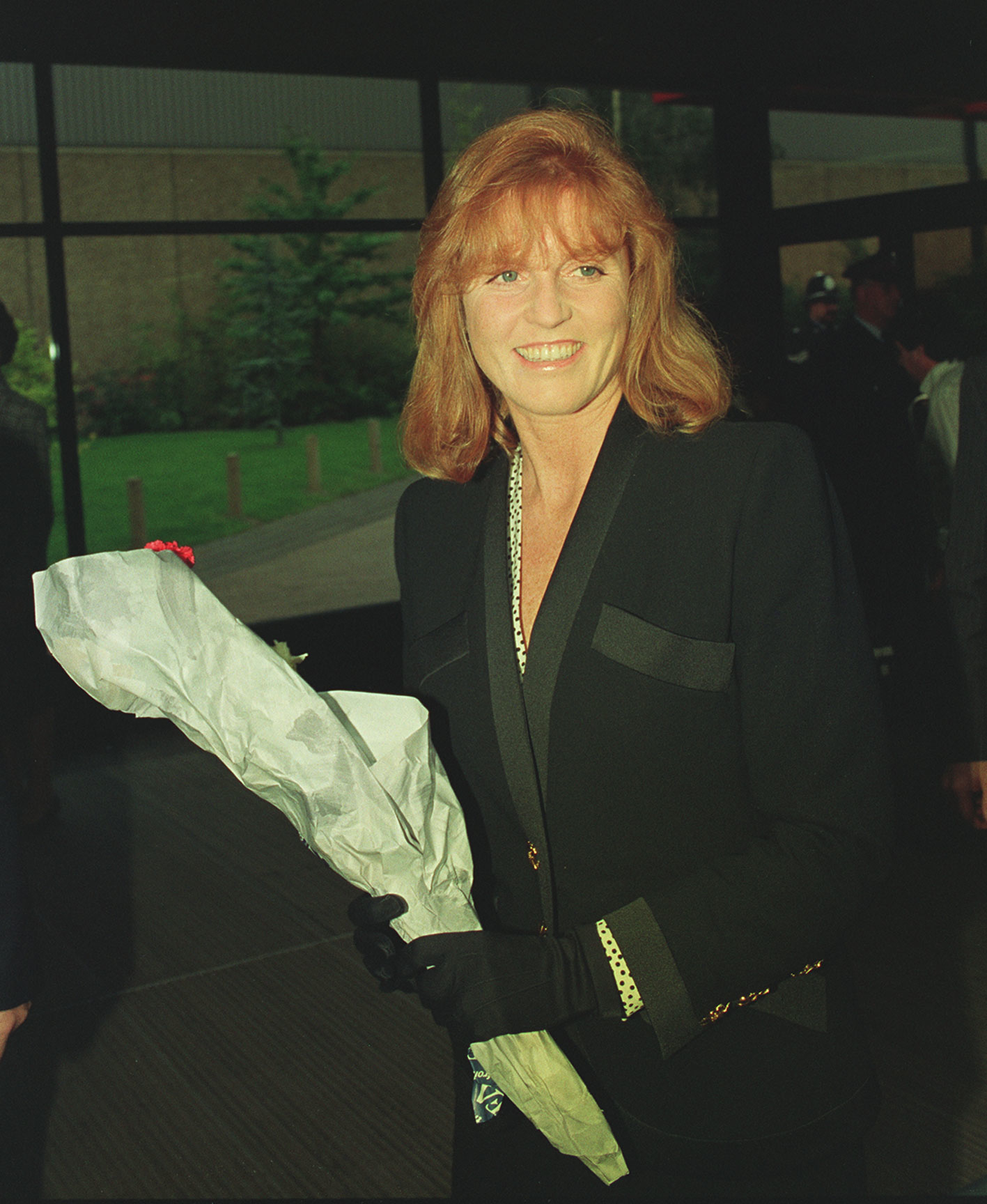 Sarah Ferguson in a black blazer, holding a bouquet, smiling at an event