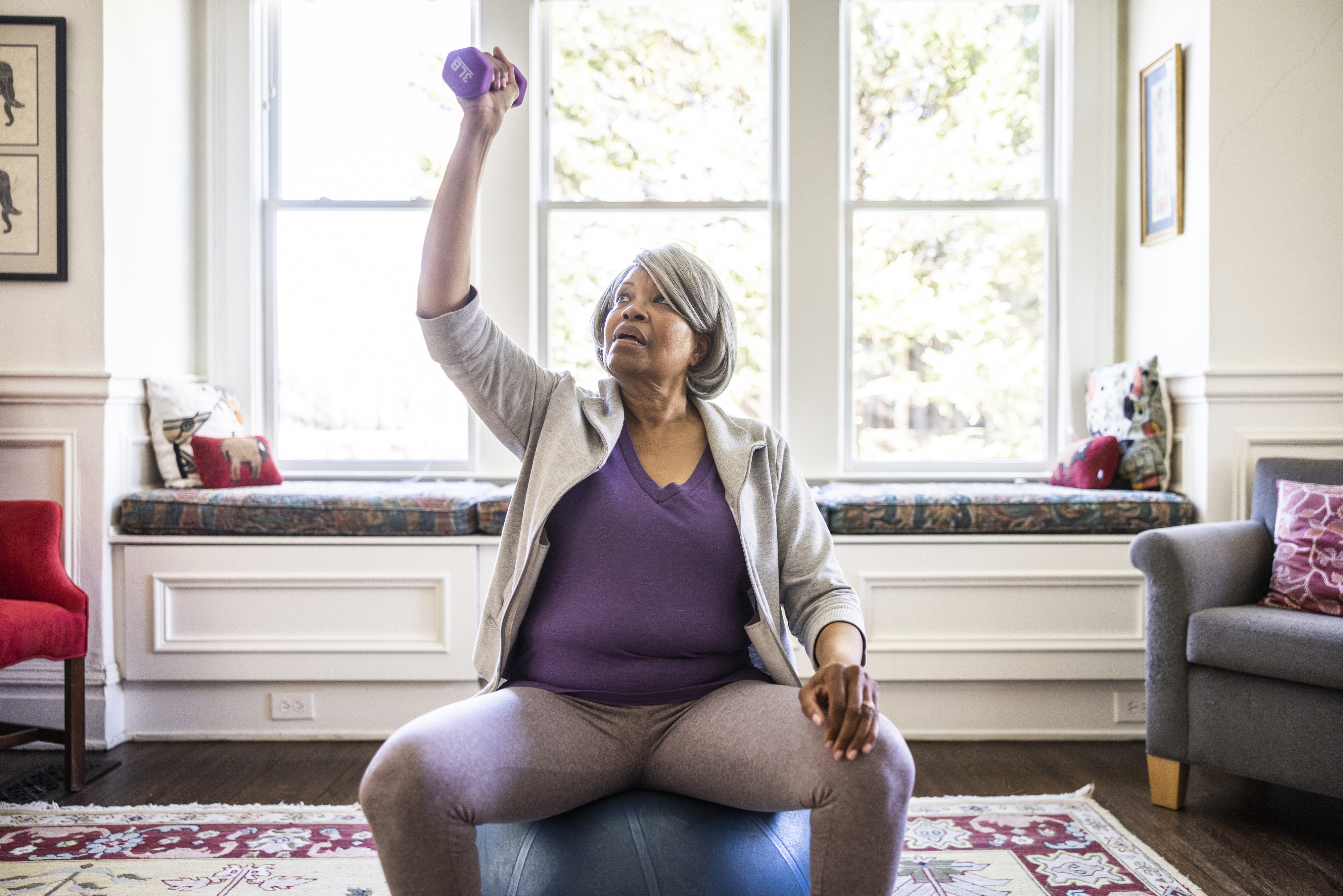Older woman exercising with dumbbell while seated in her living room