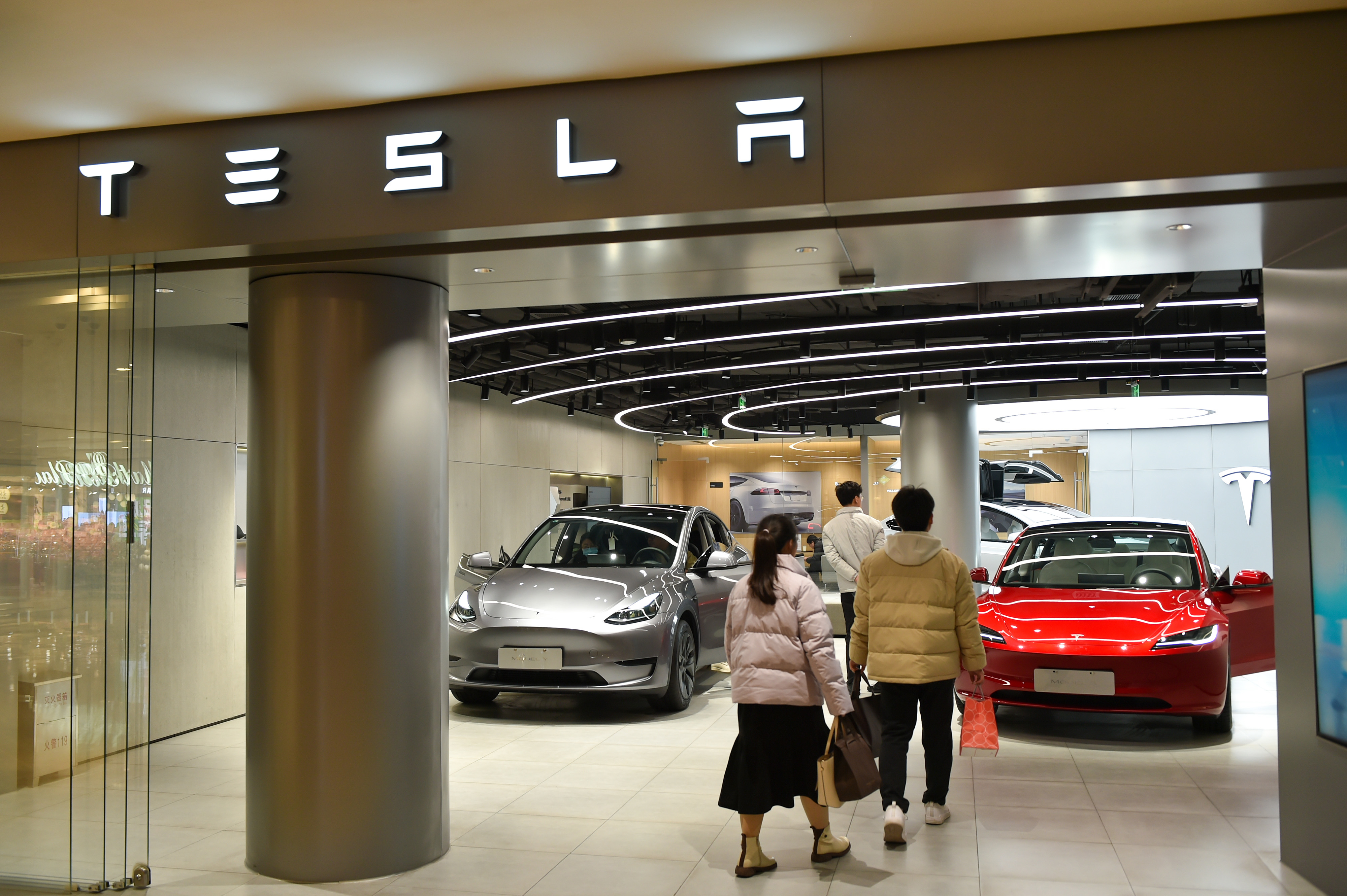 Three people walking into a Tesla showroom with multiple cars on display
