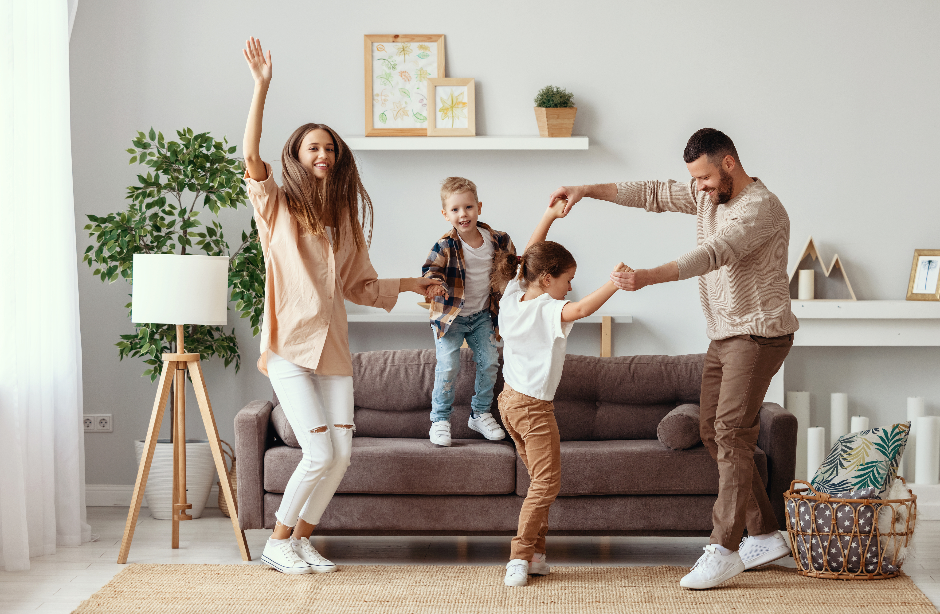 Family of four happily dancing together in a living room